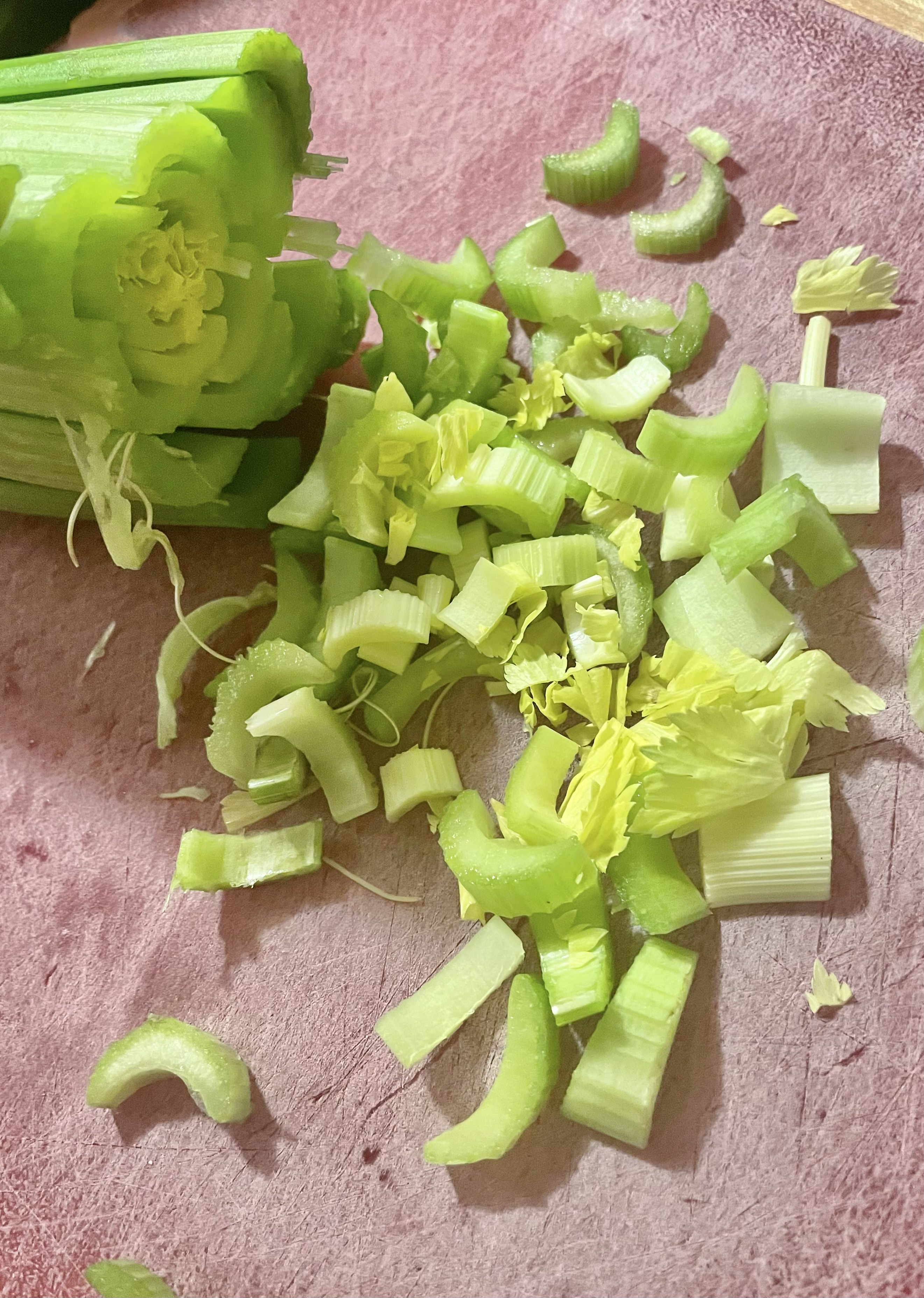 Thinly slicing celery stalk (leaves and all) on red cutting board.