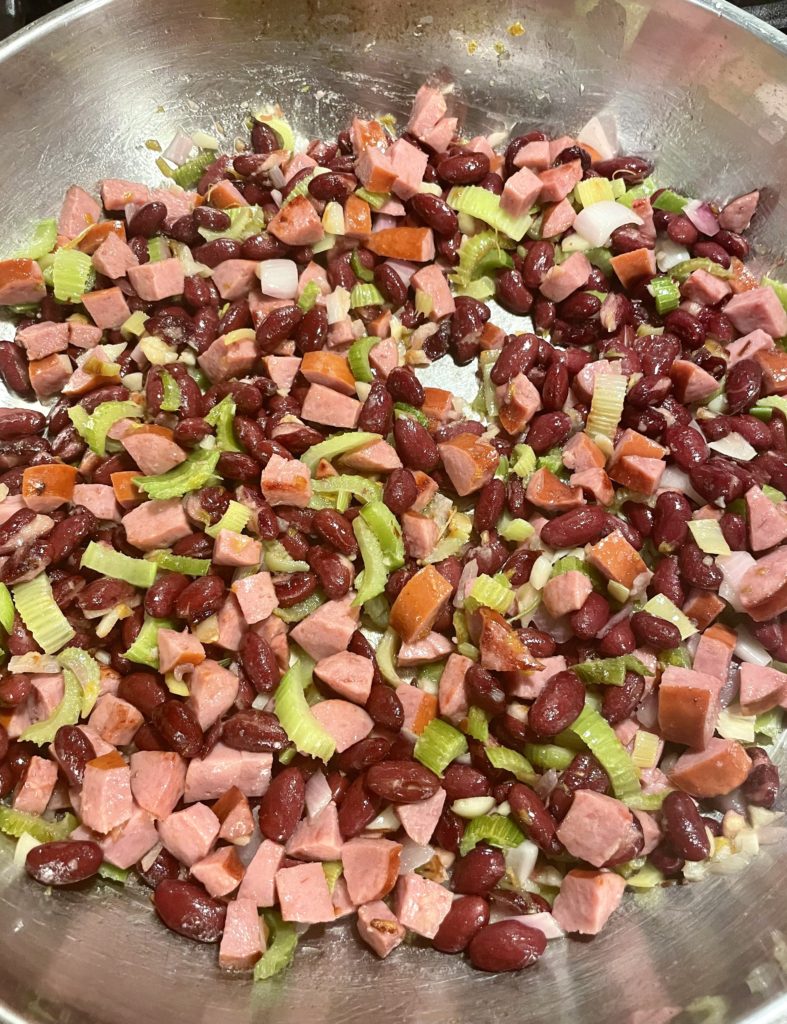 Large skillet with kielbasa, celery, garlic, purple onion and red beans frying in vegetable oil.