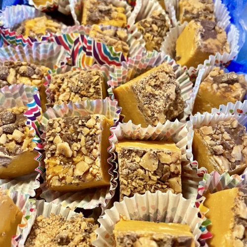 Squares of butterscotch toffee Heath fudge in mini liners boxed and surrounded with blue tissue paper.