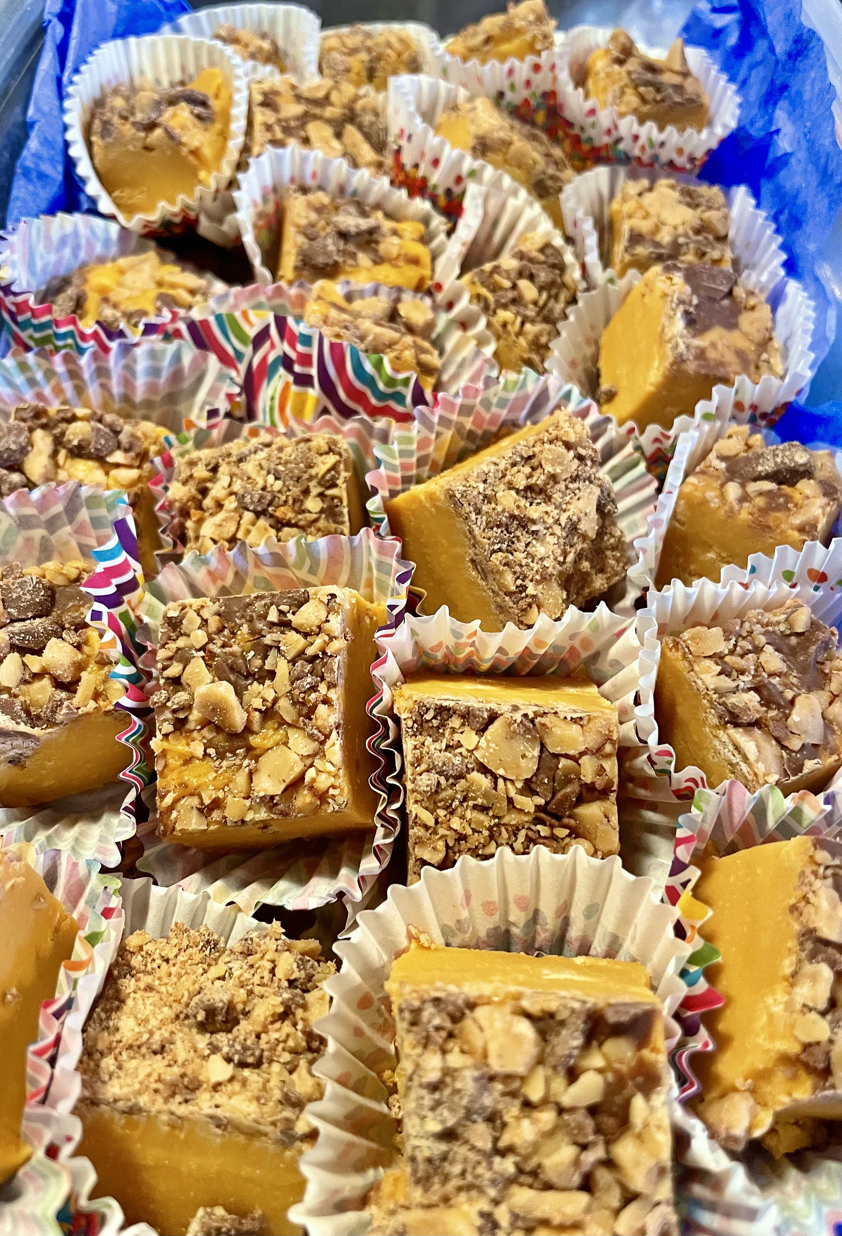 Squares of butterscotch toffee Heath fudge in mini liners boxed together and surrounded by blue tissue paper.