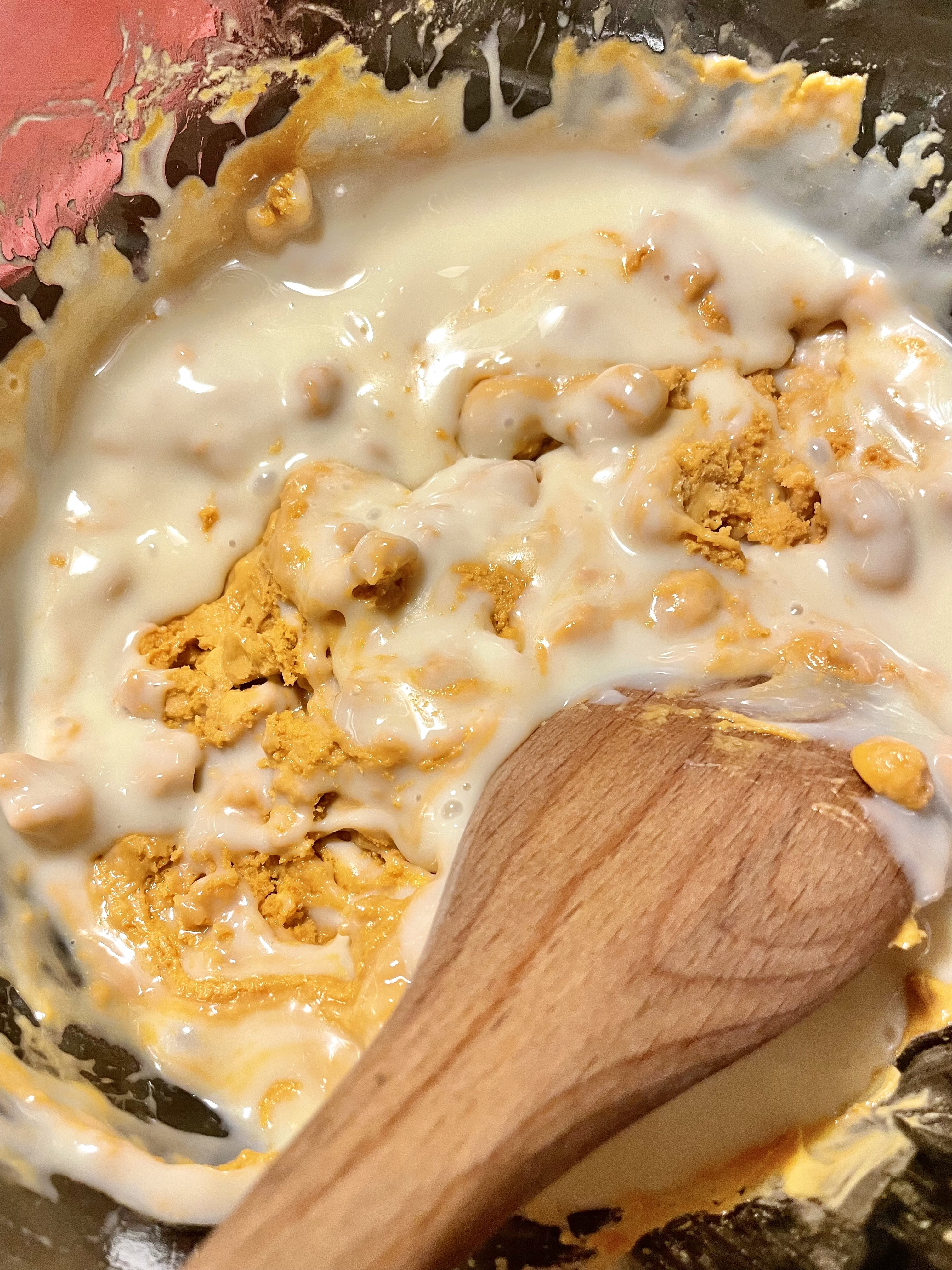 Sweetened condensed milk is being stirred into melted butterscotch chips in a double boiler.