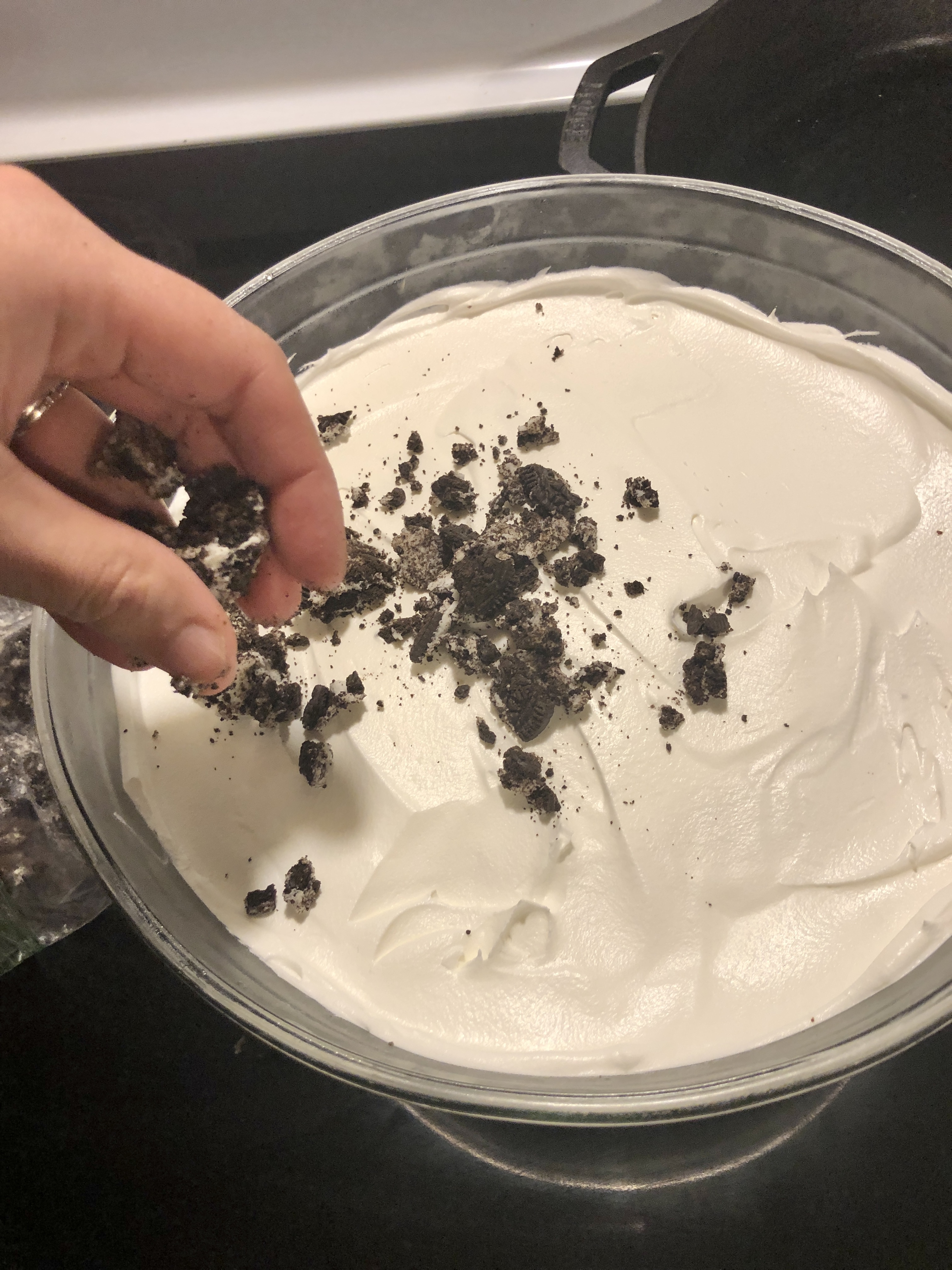 Topping Cool Whip in trifle bowl with crushed Oreo cookies.