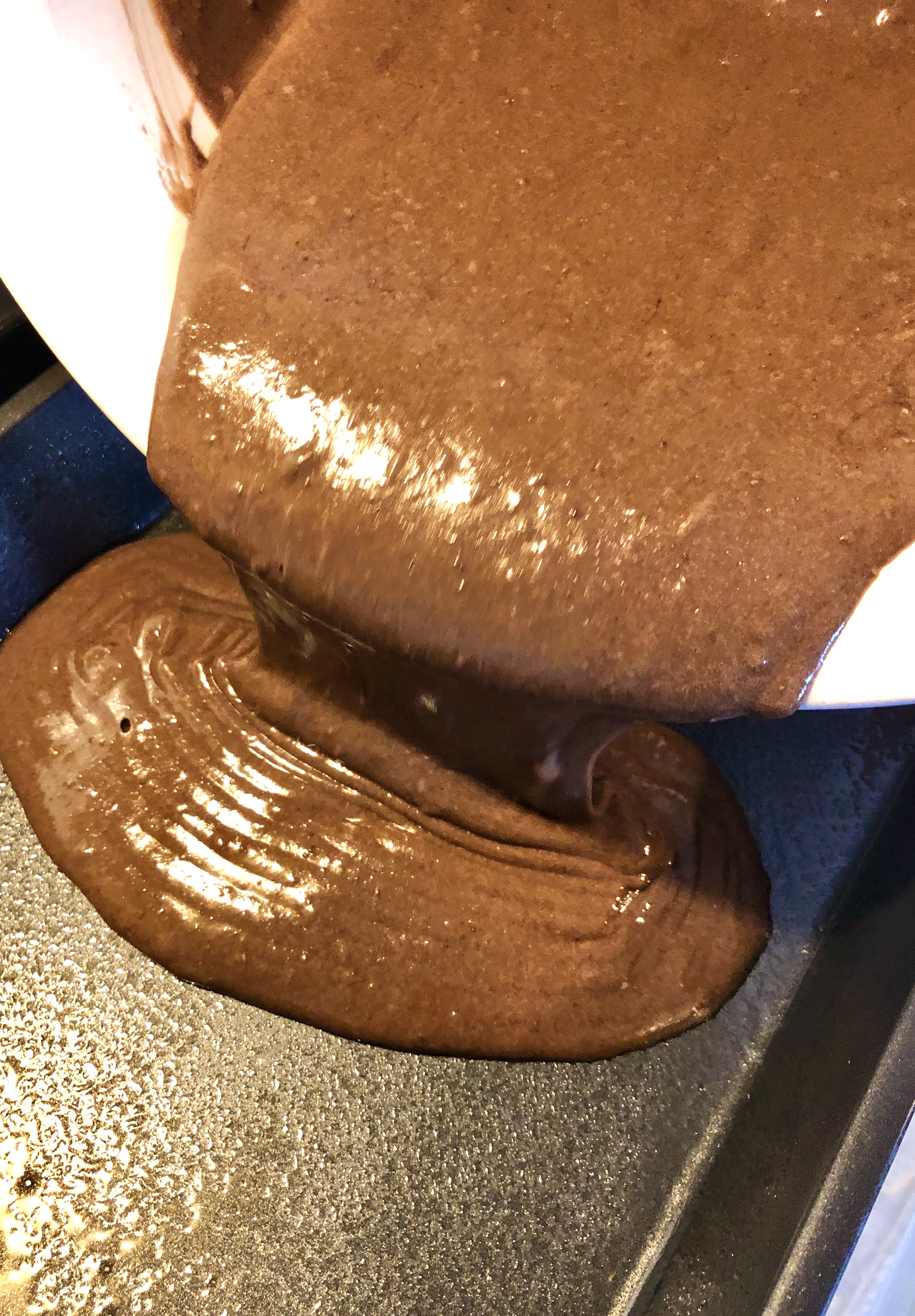 Chocolate box cake mix batter being poured from large white mixing bowl into a greased 13x9 baking pan.