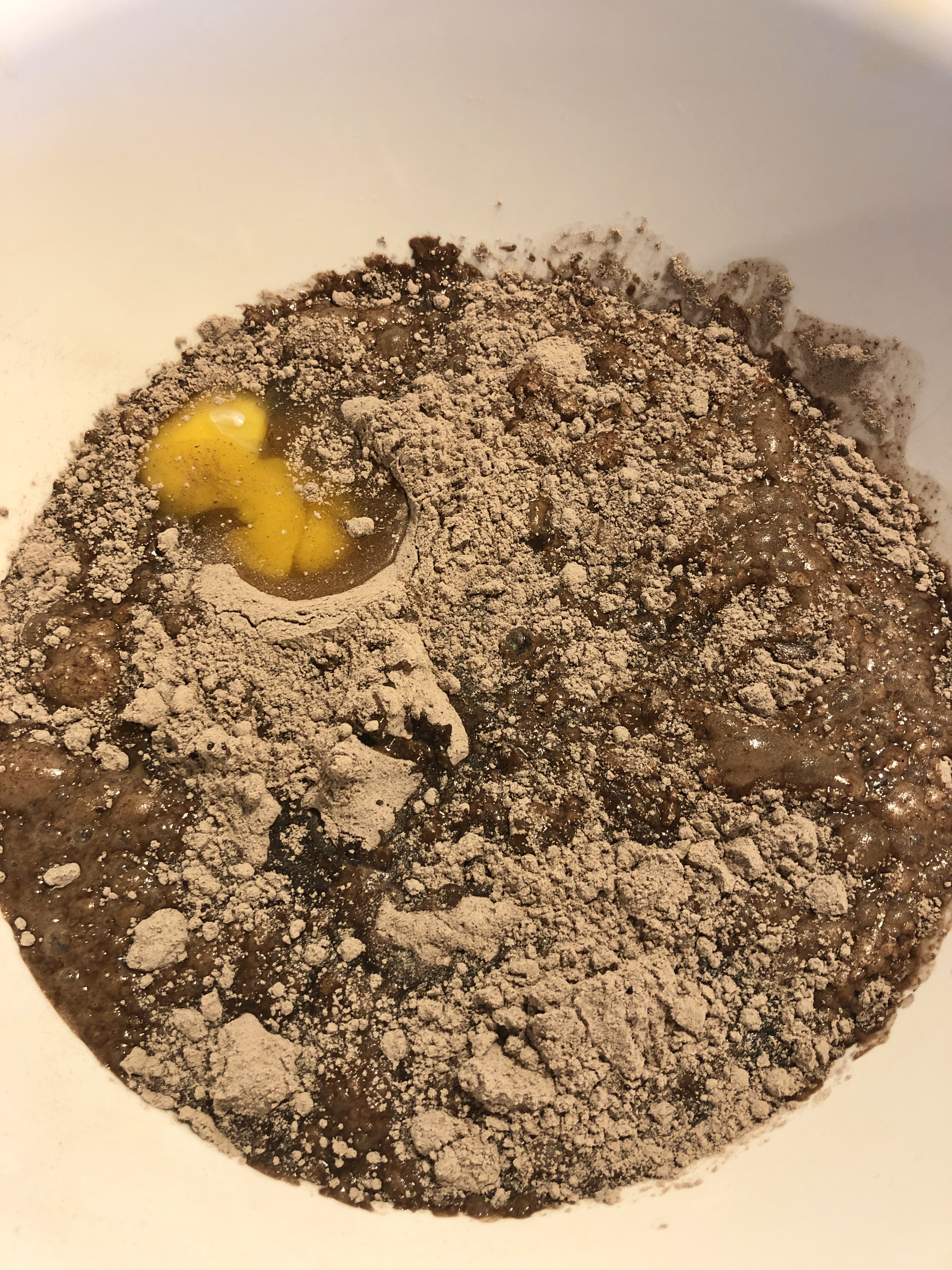 Boxed chocolate cake mix being prepared in large white mixing bowl. Egg, vegetable oil and water have been added to the bowl.