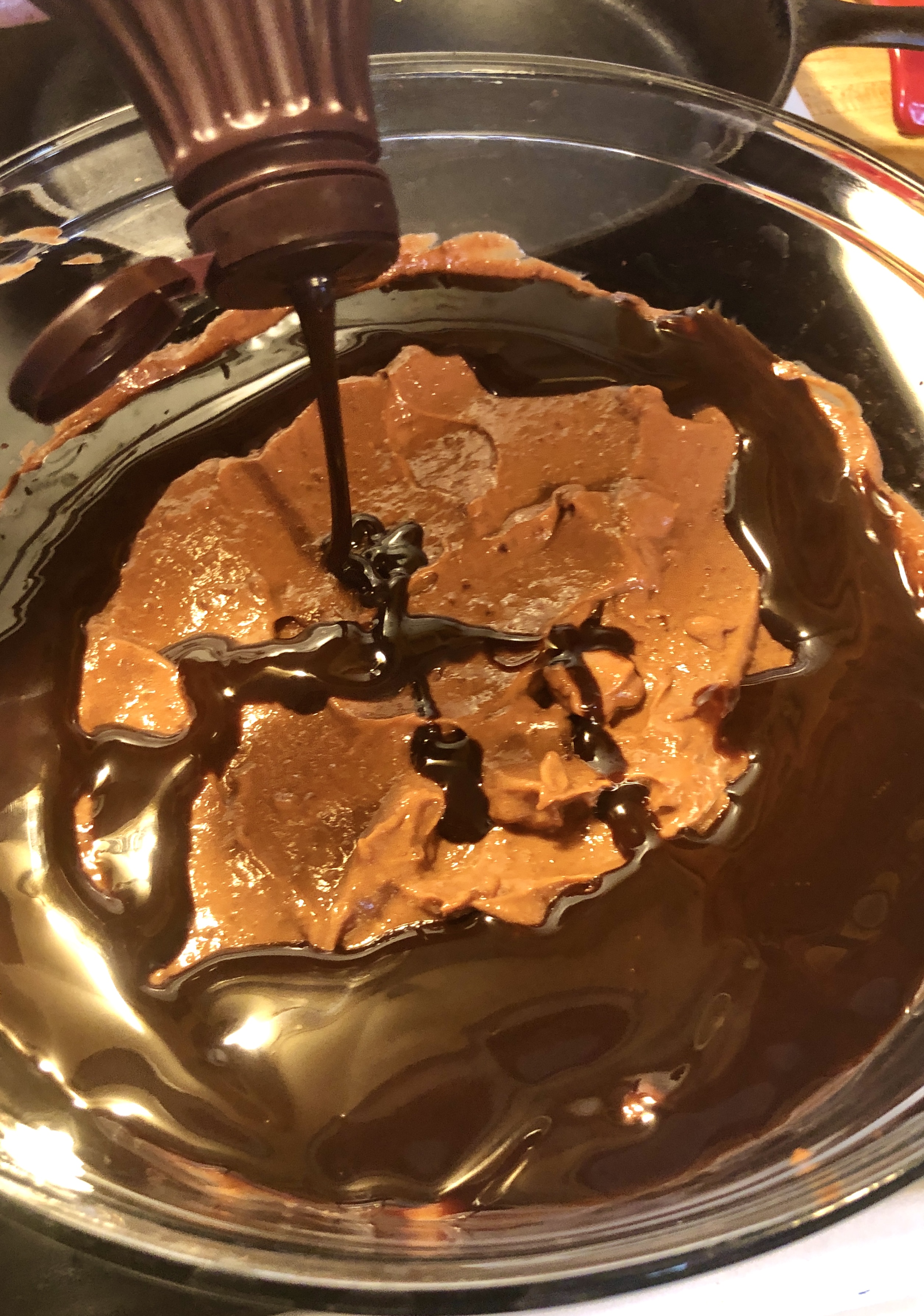 Chocolate syrup being added over the top of chocolate pudding in a trifle bowl.