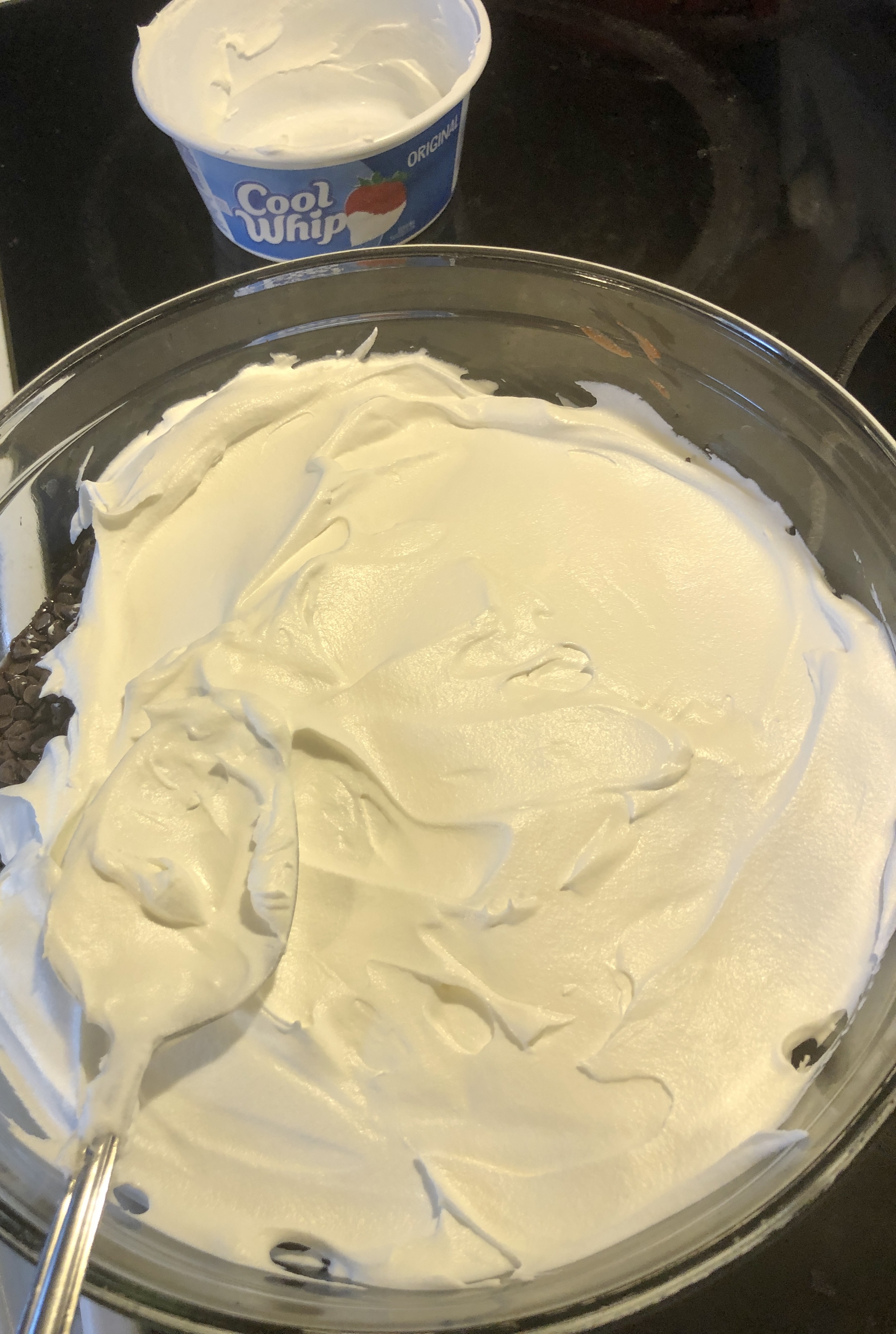 Cool whip being spread over the top of Dirt Cake dessert in trifle dish.