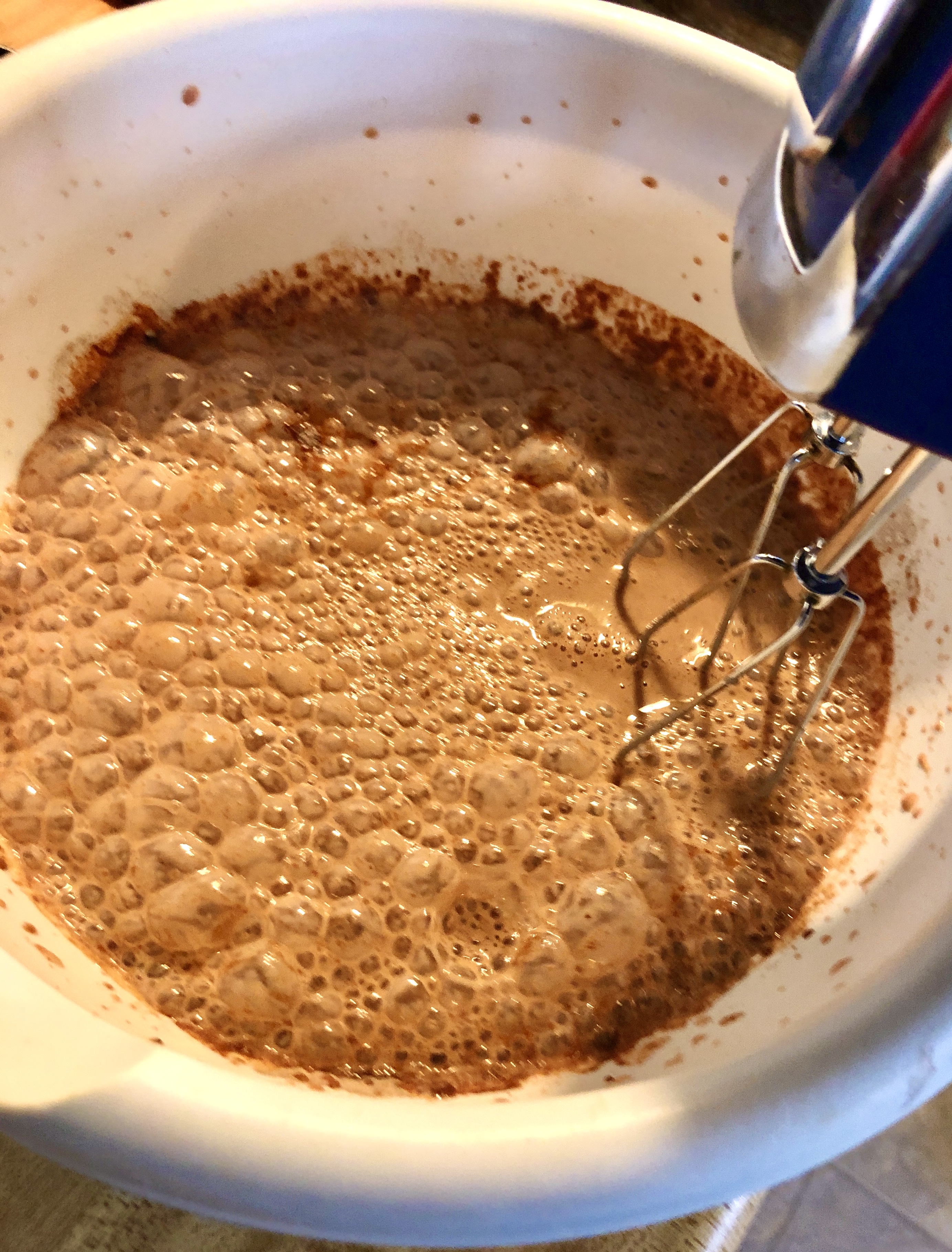 Instant chocolate pudding mix being mixed with an electric mixer in a white mixing bowl.