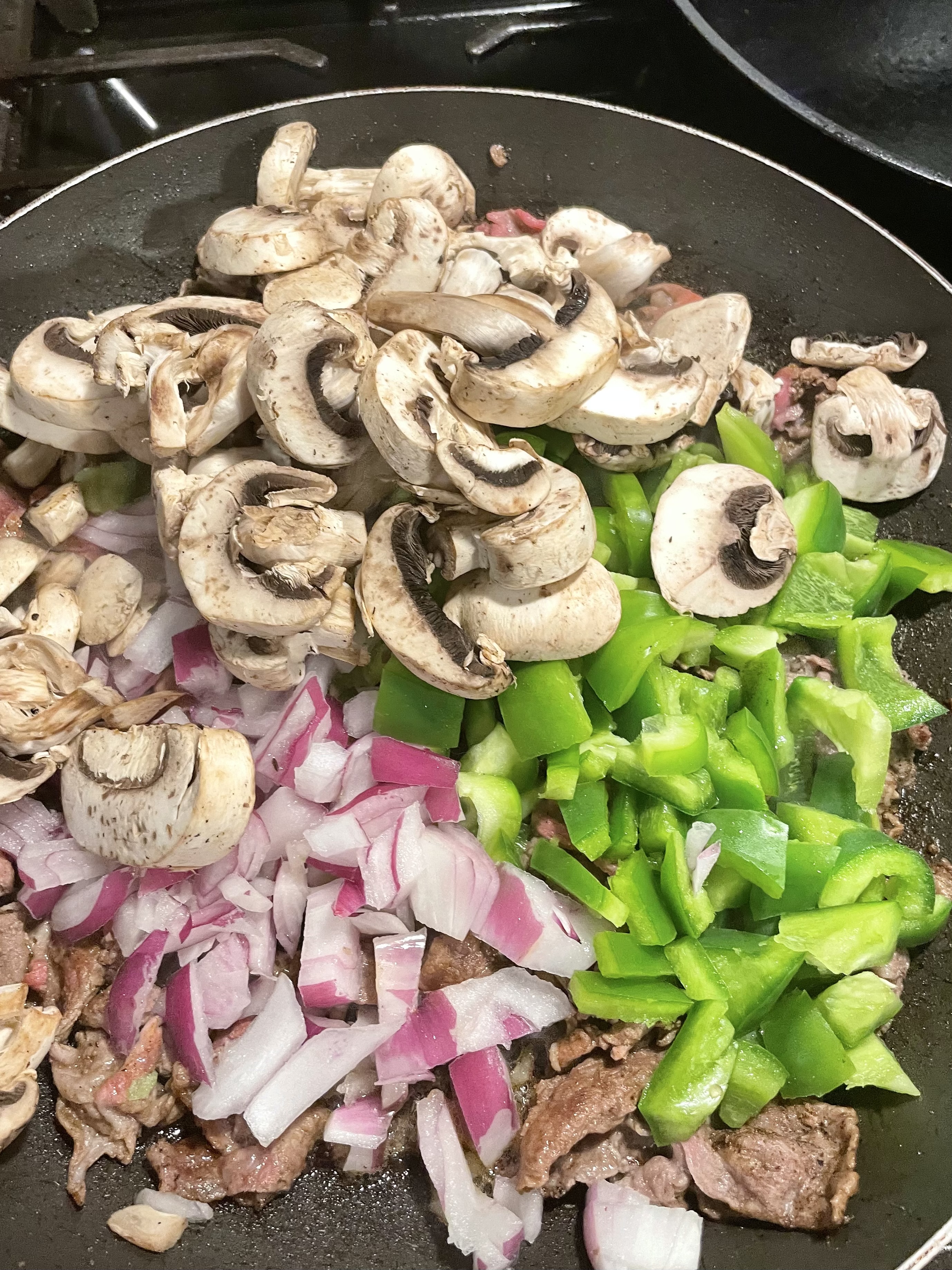 Fresh chopped mushroom, green pepper and onion added to pan of frying shaved steak.