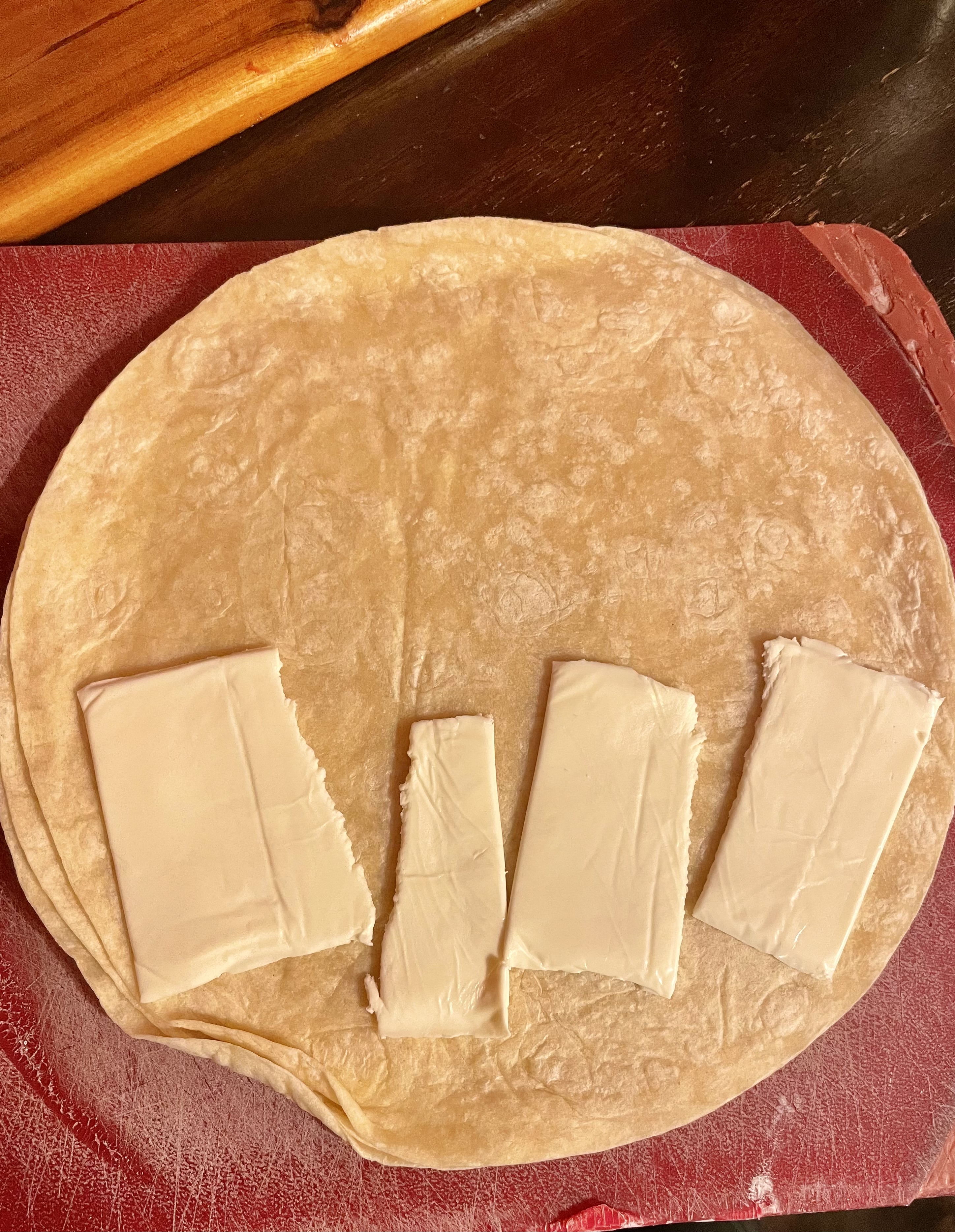 Flour tortilla on red cutting board with torn pieces of American cheese covering half of the tortilla.