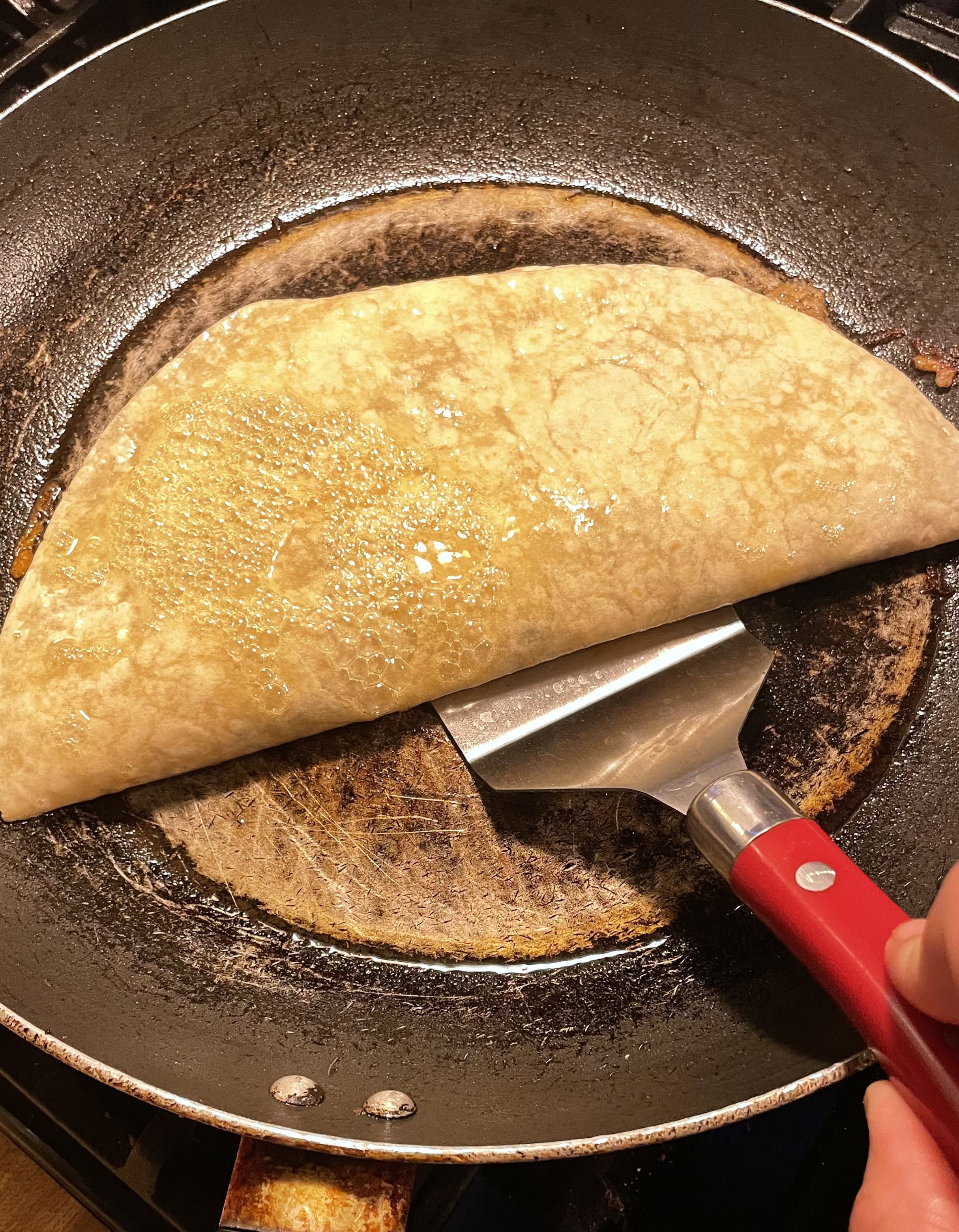 Quesadilla in pan being flipped with spatula. The top has been pan sprayed.