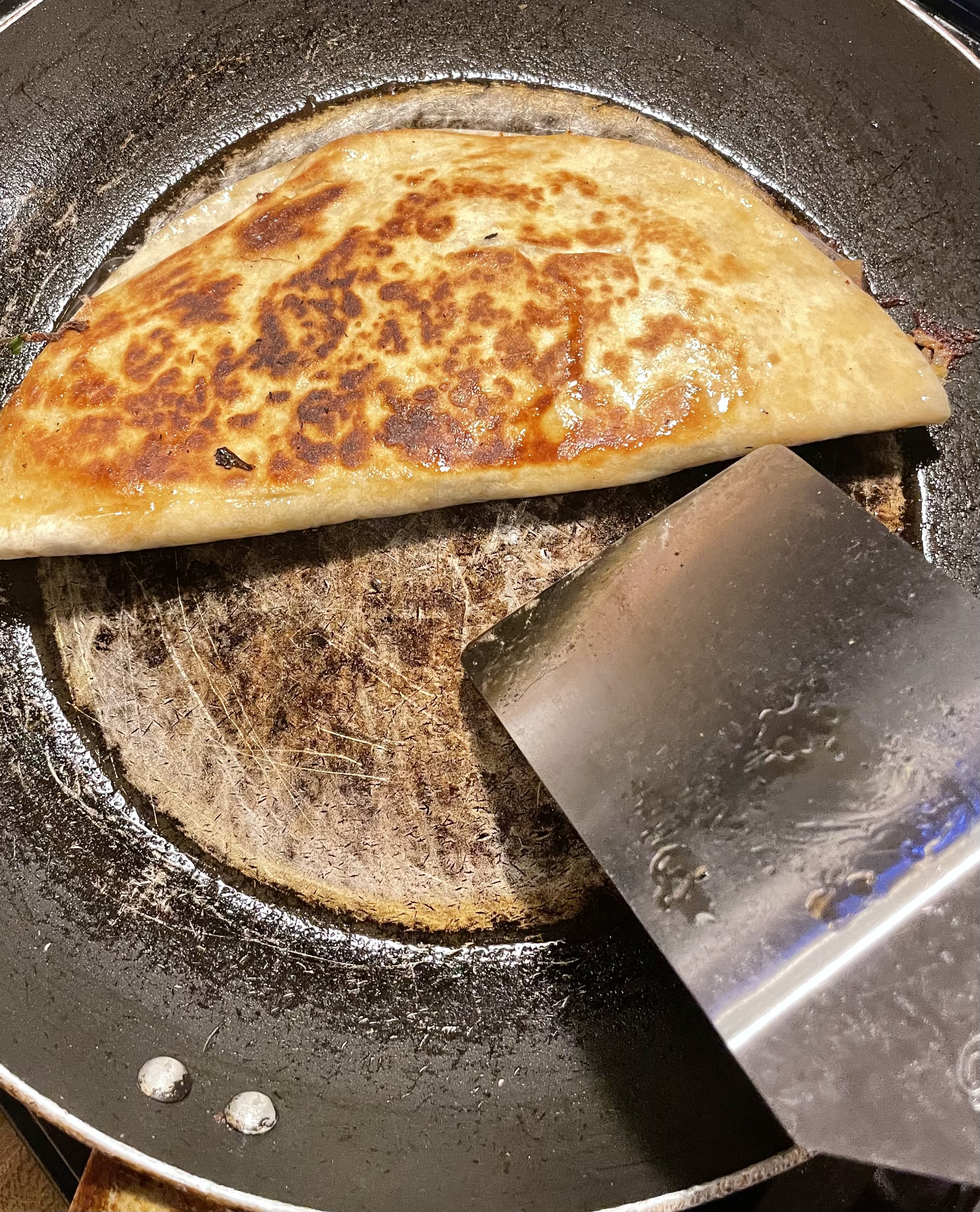 A cooking quesadilla has been flipped in a frying pan.