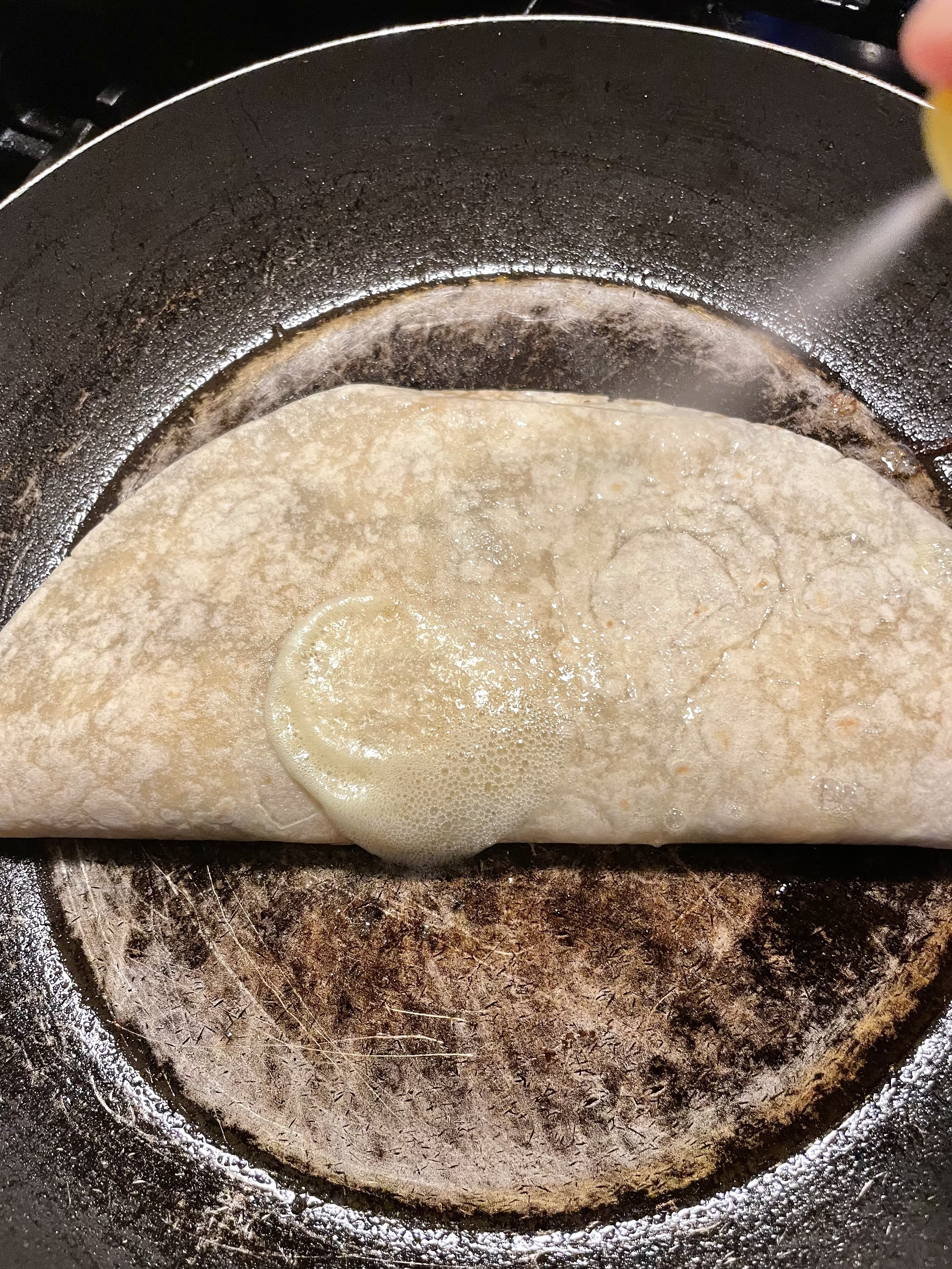 Pan spraying the top of a steak bomb quesadilla before flipping it over in the skillet.