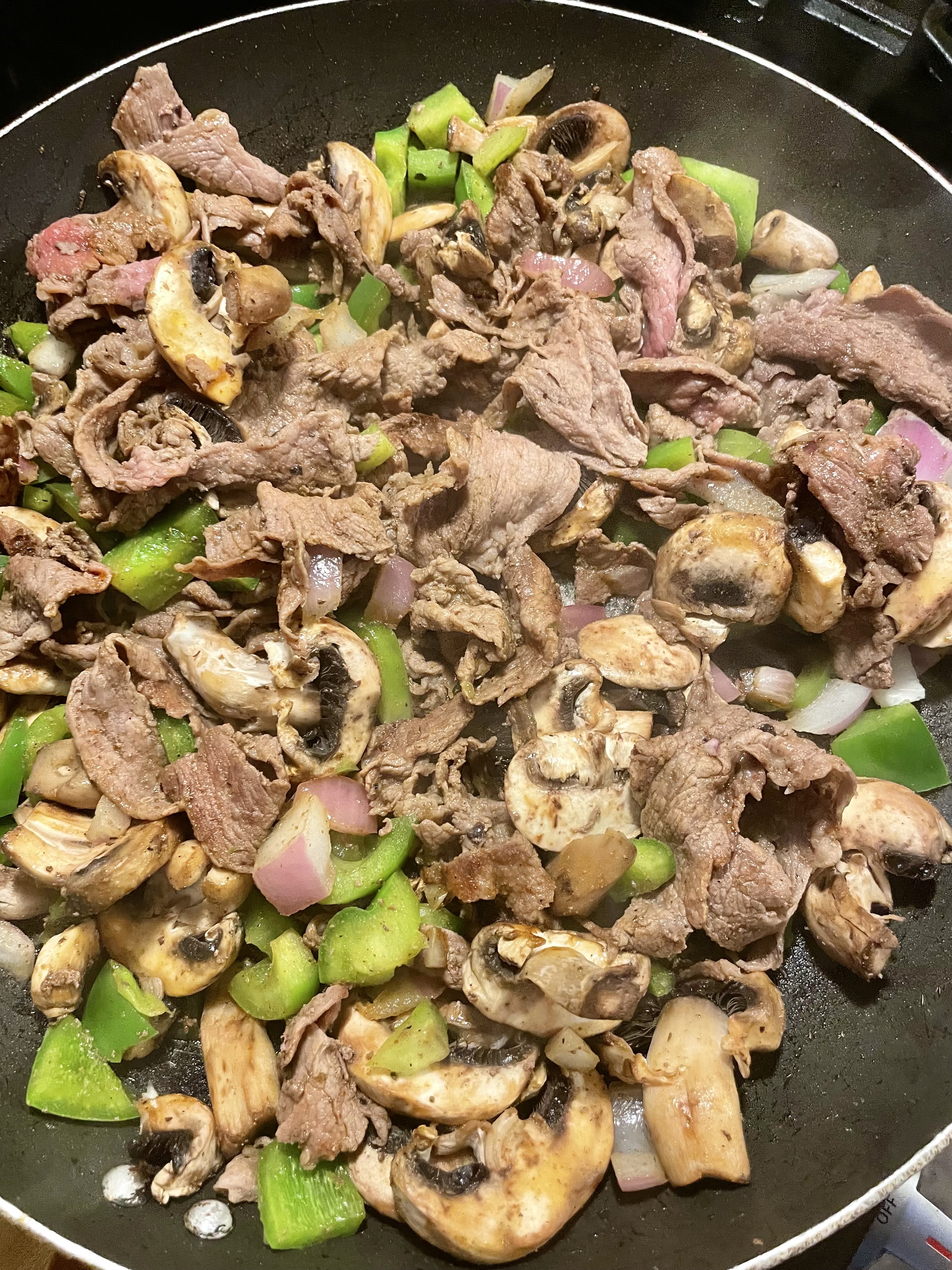 Stirring shaved steak, mushroom, pepper and onion in skillet.