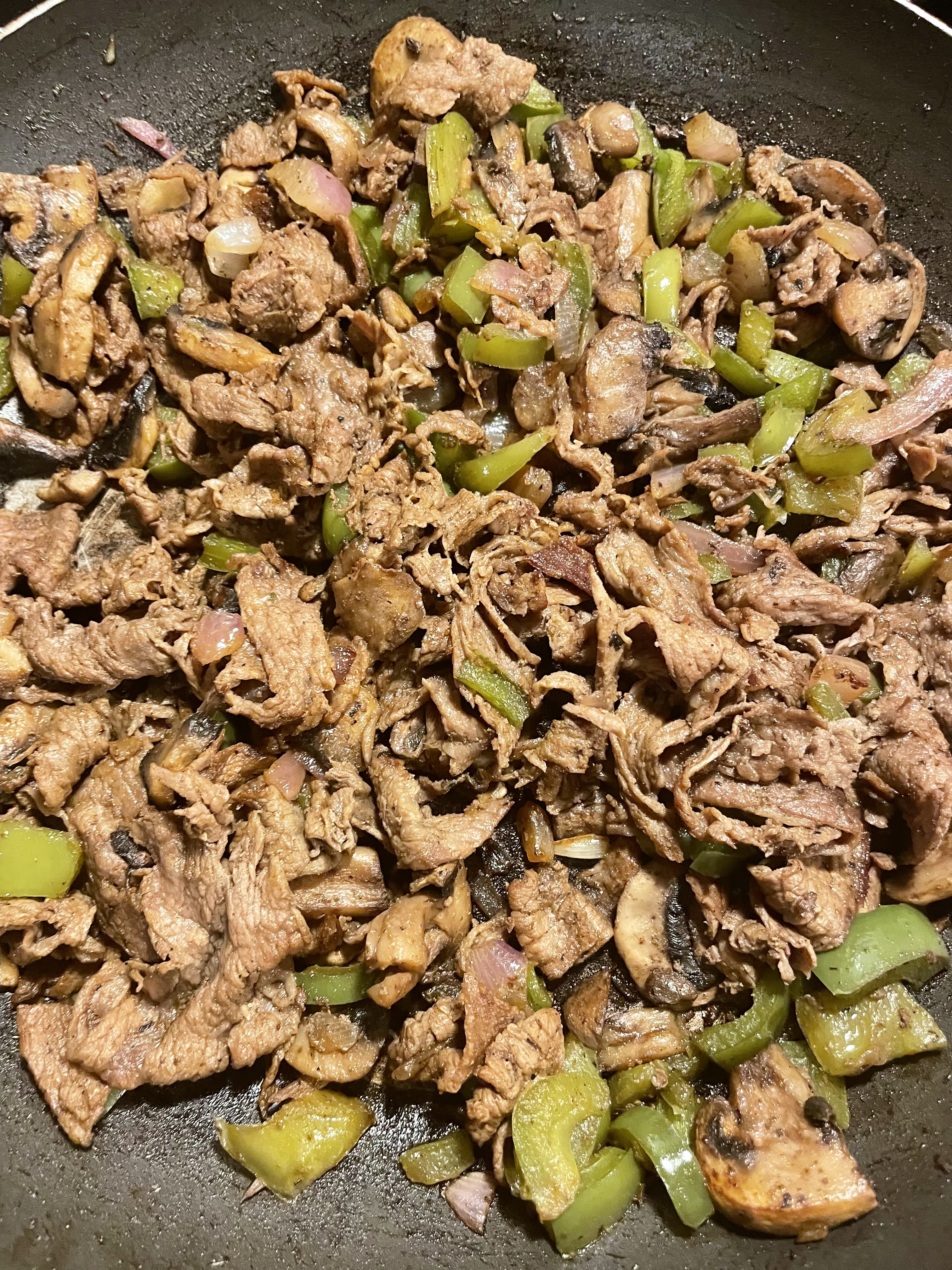 Cooked steak bomb filling in skillet on stovetop.