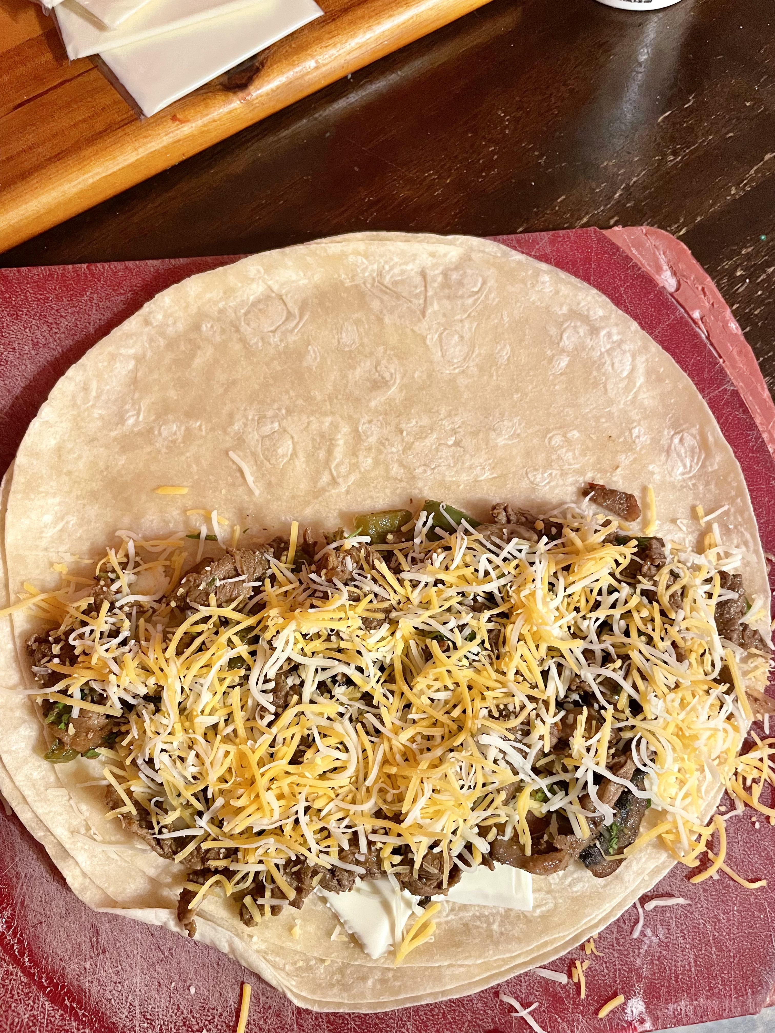 Steak bomb quesadilla being assembled with the final layer of taco cheese added to the top.