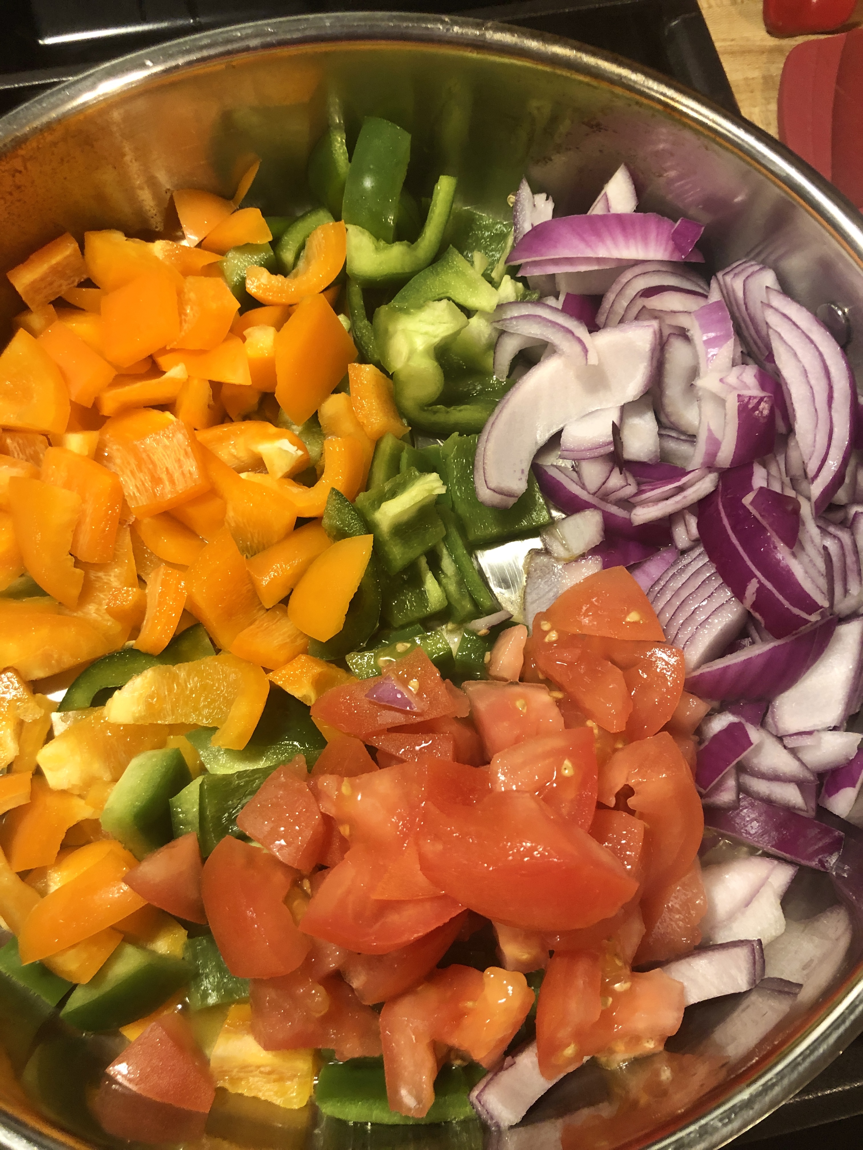 Orange and green bell peppers, tomato, garlic and purple onion in frying pan.