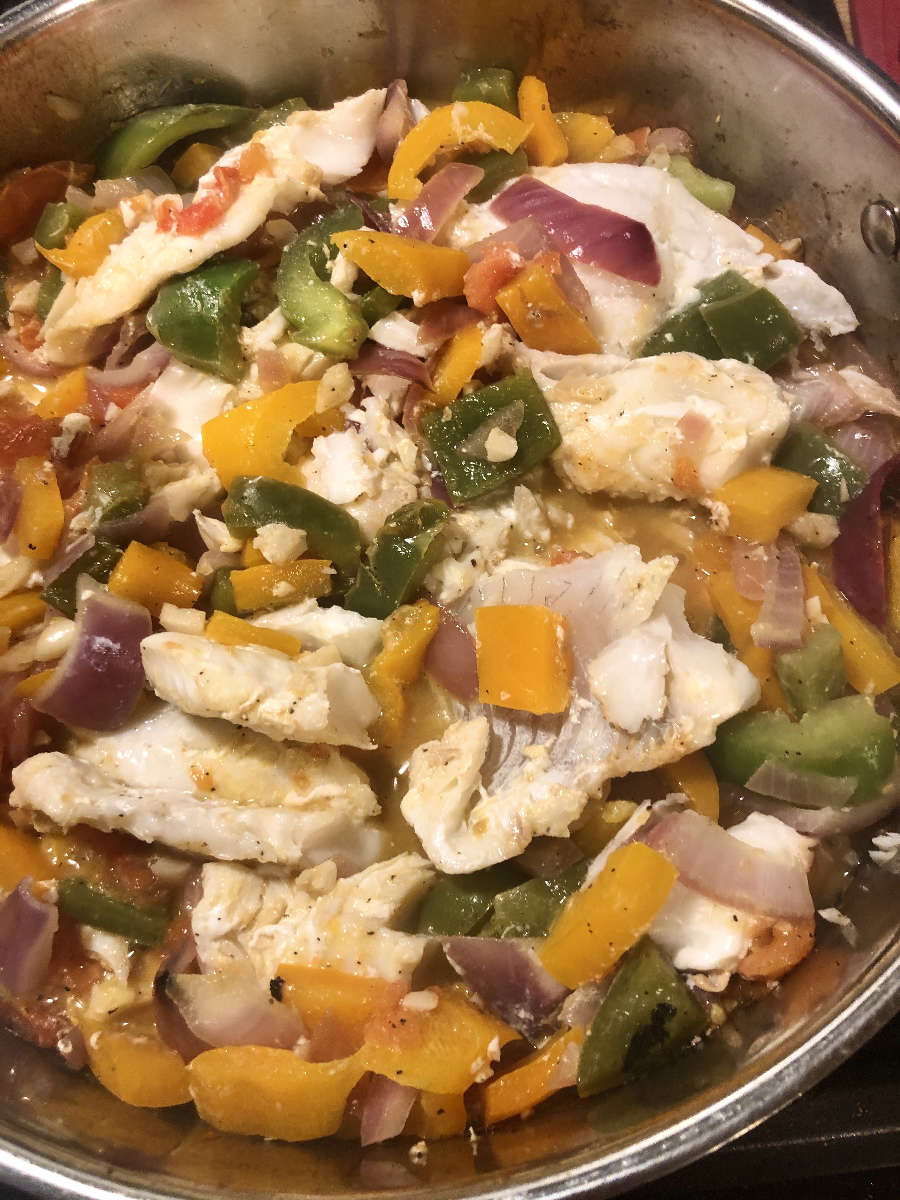 Haddock breaking apart in frying pan while cooking with vegetables.