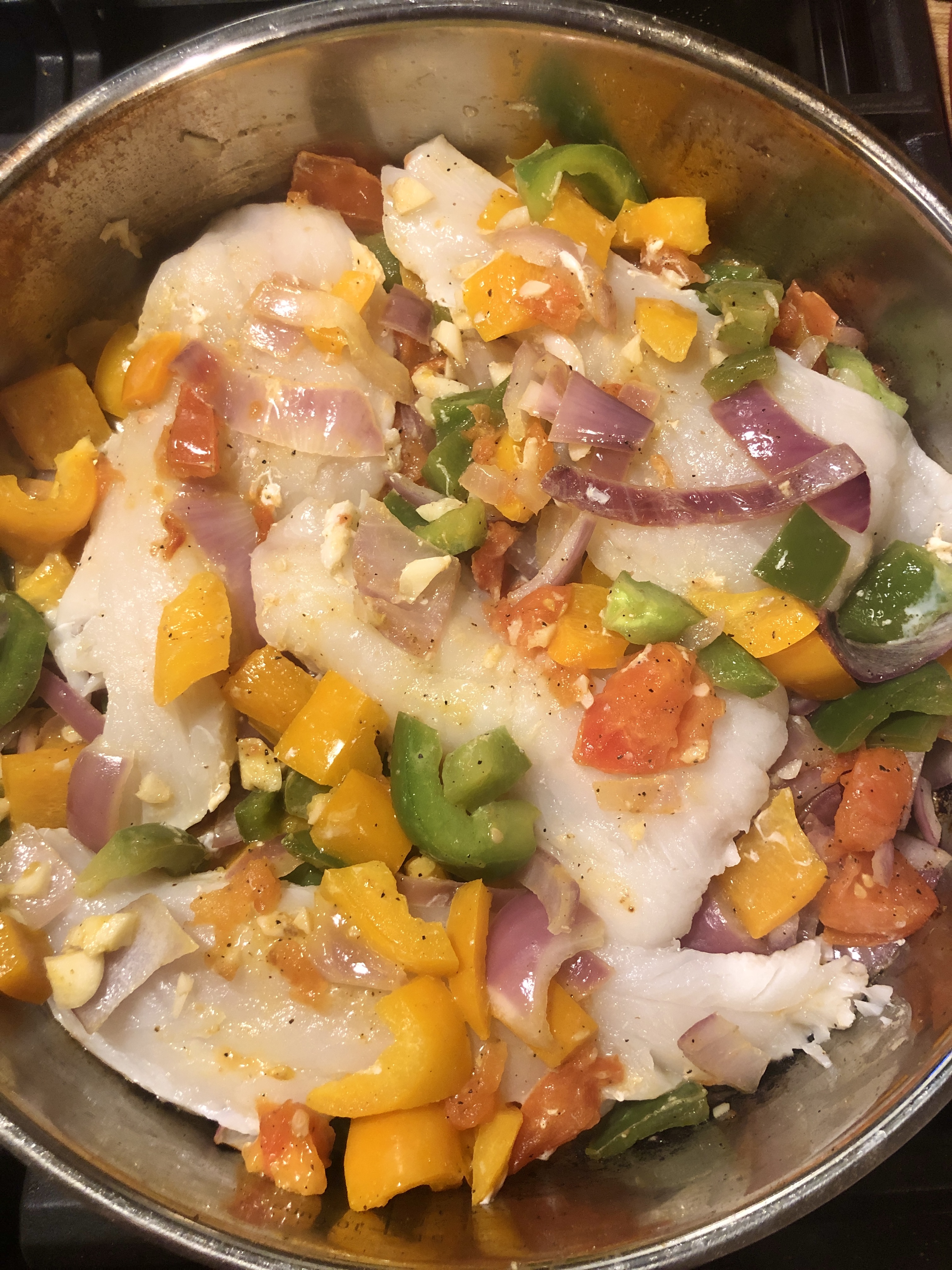Covering haddock with vegetables cooking in a frying pan.