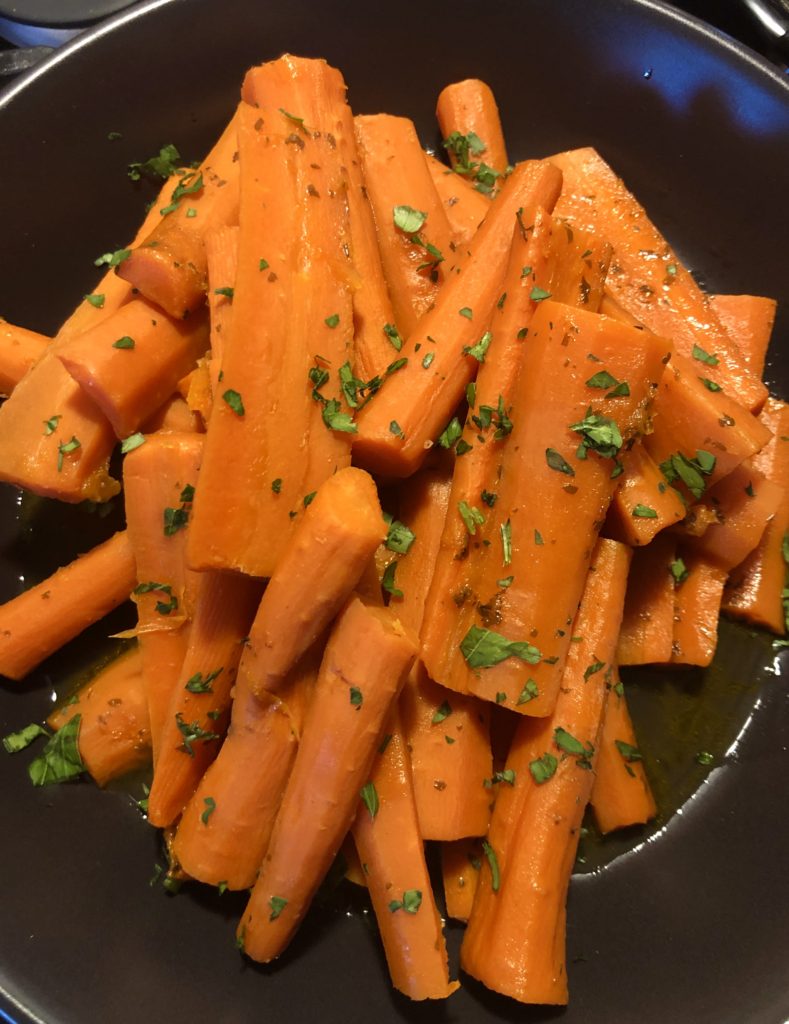 Orange Apricot Glazed Carrots pictured in a black bowl and garnished with fresh parsley.