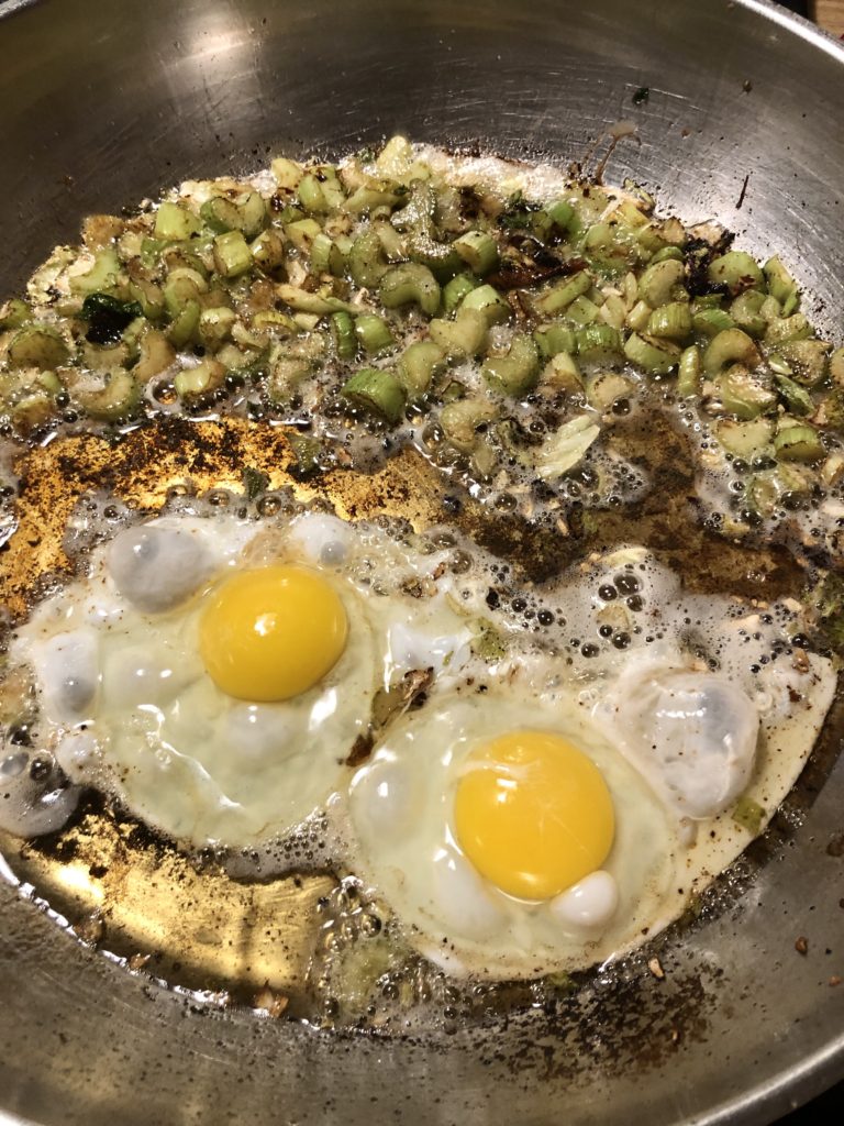 Two eggs sunny side up in a frying pan beside celery.