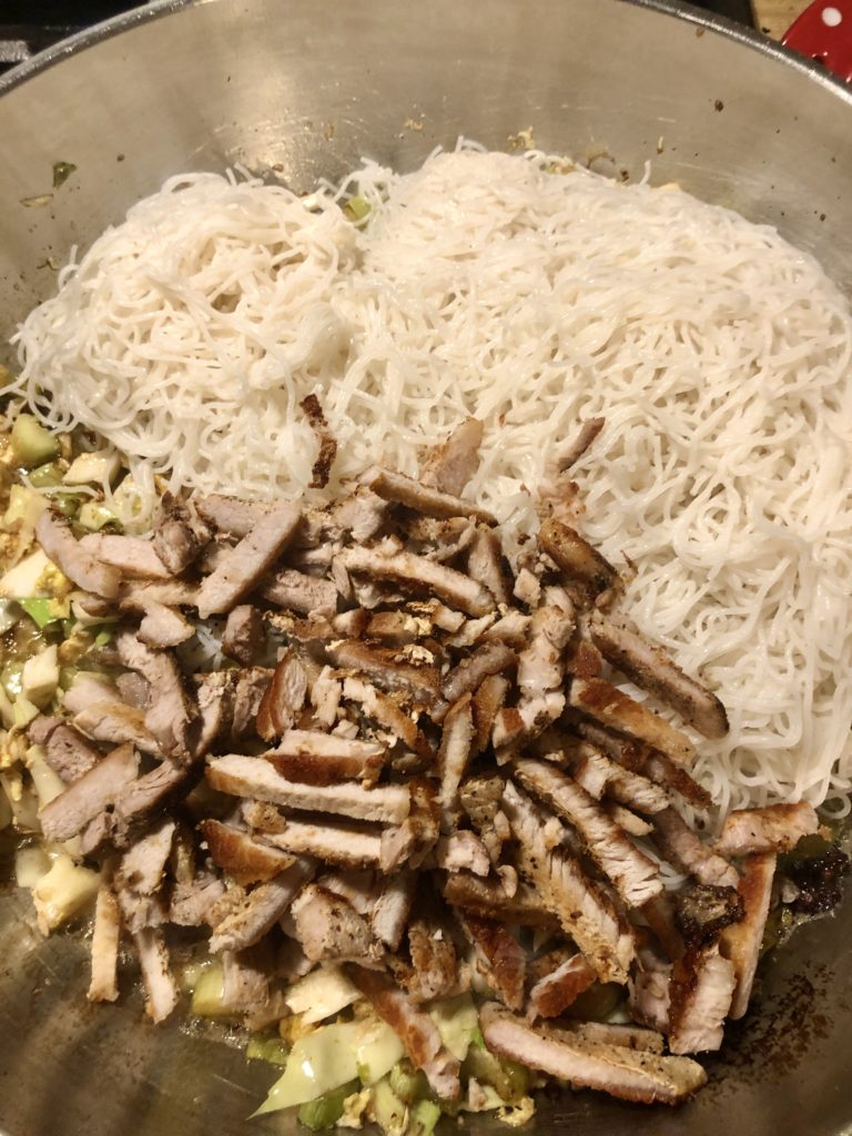 Cooked rice noodles and cooked sliced pork added to frying pan.