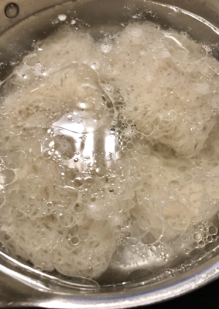 Preparing rice vermicelli noodles according to package instructions by boiling in a pan.