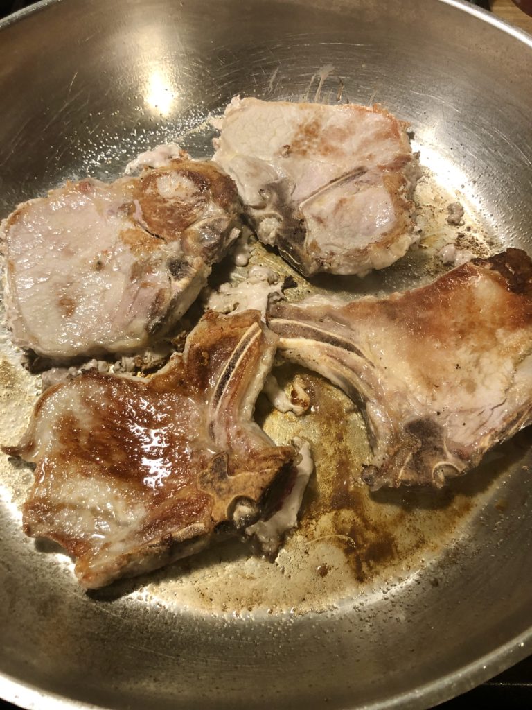 Four pork chops frying and browning in large skillet.