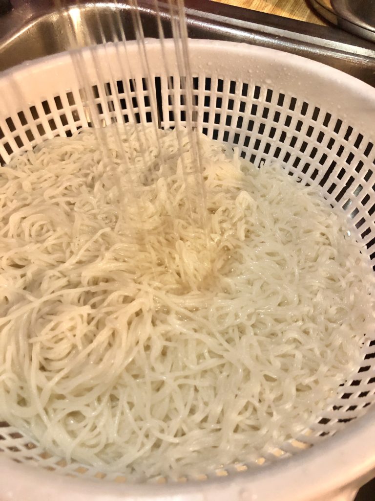 Draining and rinsing cooked rice vermicelli noodles under cold water.