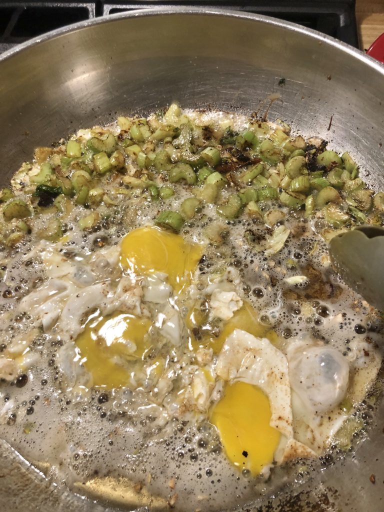 Scrambling two eggs added to a large skillet with celery cooking in it.