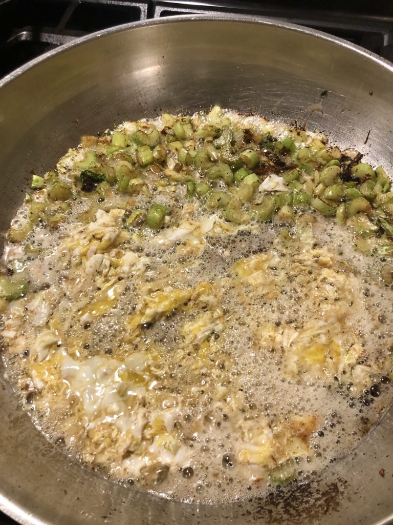 Scrambled eggs and celery frying in vegetable oil in large skillet.