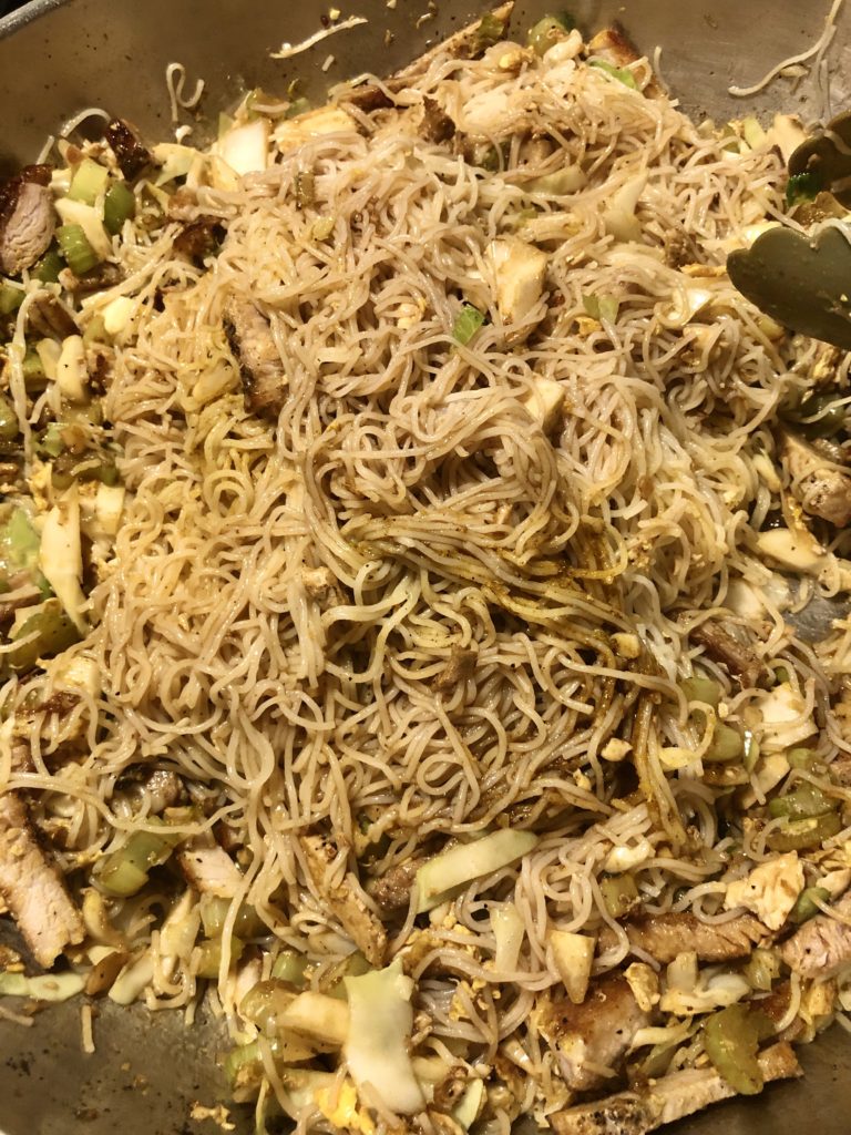 Singapore noodles being mixed in a large skillet.
