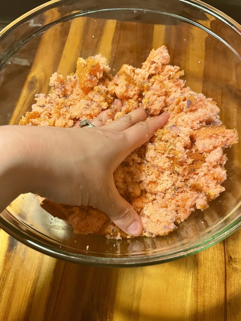 Pushing down and packing in baked strawberry cake into the bottom of a trifle dish.